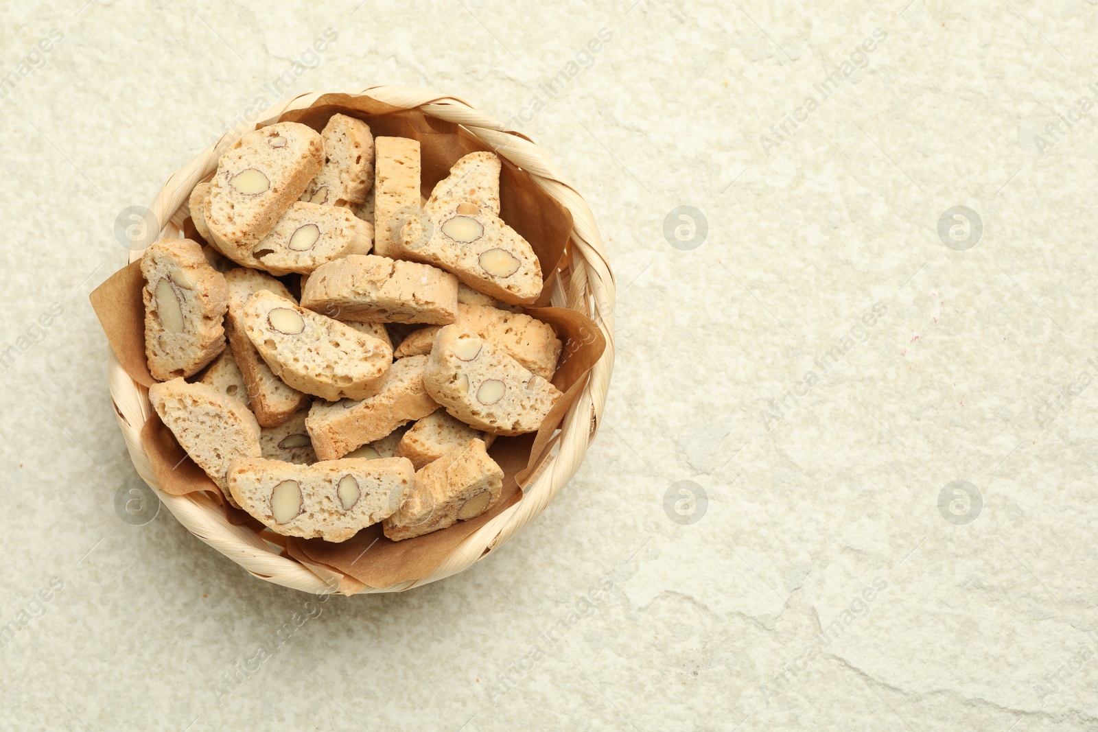 Photo of Traditional Italian almond biscuits (Cantucci) in wicker bowl on light textured table, top view. Space for text