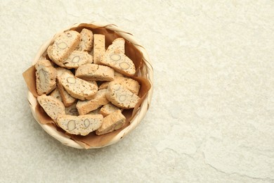 Traditional Italian almond biscuits (Cantucci) in wicker bowl on light textured table, top view. Space for text