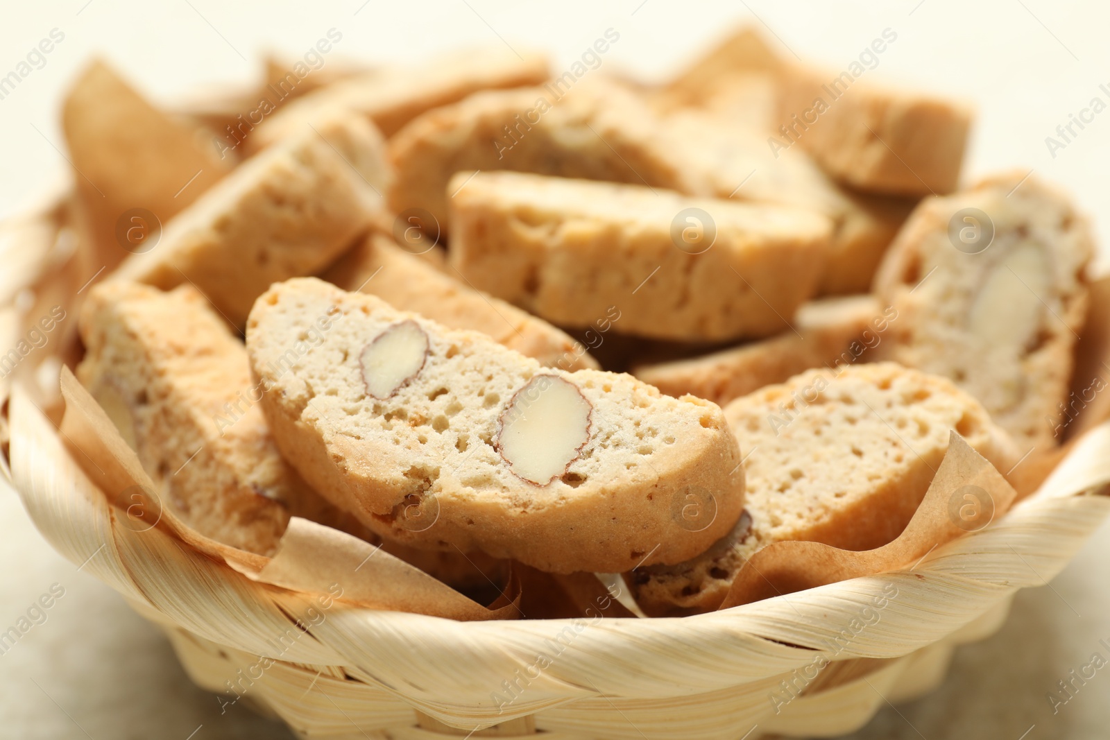 Photo of Traditional Italian almond biscuits (Cantucci) in wicker bowl on light table, closeup