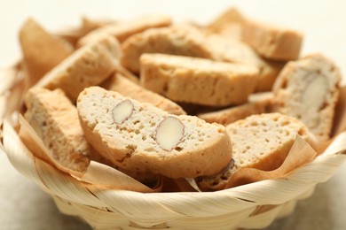 Traditional Italian almond biscuits (Cantucci) in wicker bowl on light table, closeup