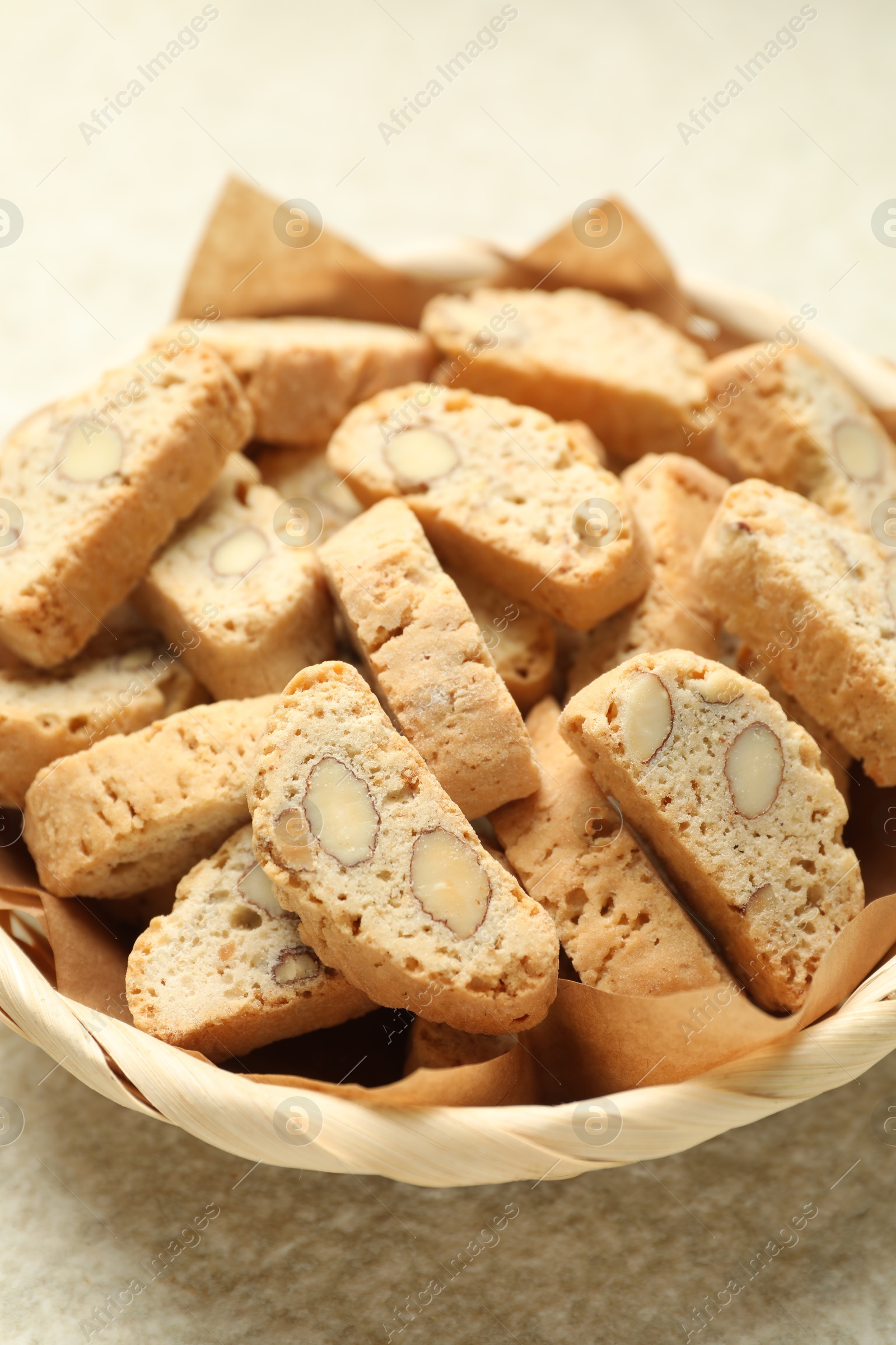 Photo of Traditional Italian almond biscuits (Cantucci) in wicker bowl on light textured table, closeup