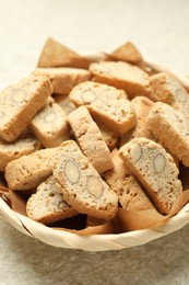 Traditional Italian almond biscuits (Cantucci) in wicker bowl on light textured table, closeup