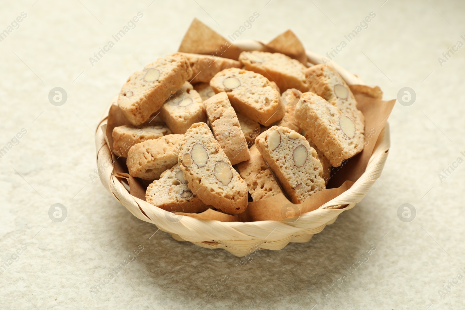 Photo of Traditional Italian almond biscuits (Cantucci) in wicker bowl on light textured table, closeup