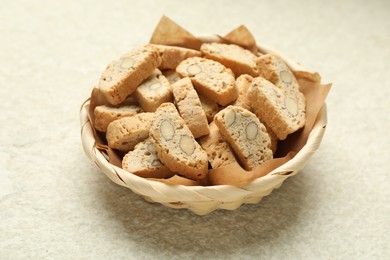 Traditional Italian almond biscuits (Cantucci) in wicker bowl on light textured table, closeup