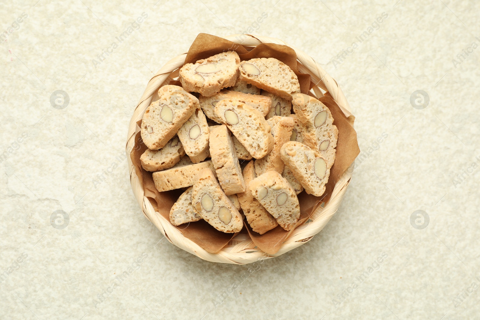 Photo of Traditional Italian almond biscuits (Cantucci) in wicker bowl on light textured table, top view