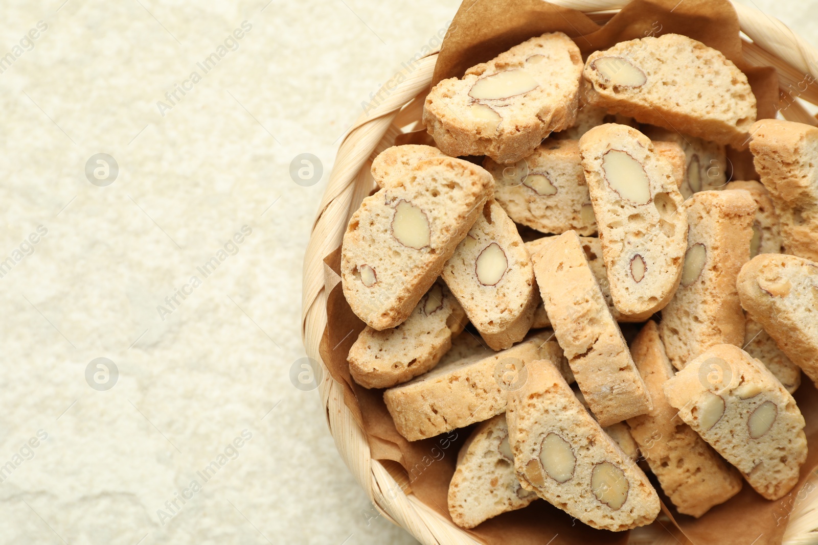 Photo of Traditional Italian almond biscuits (Cantucci) in wicker bowl on light textured table, top view. Space for text