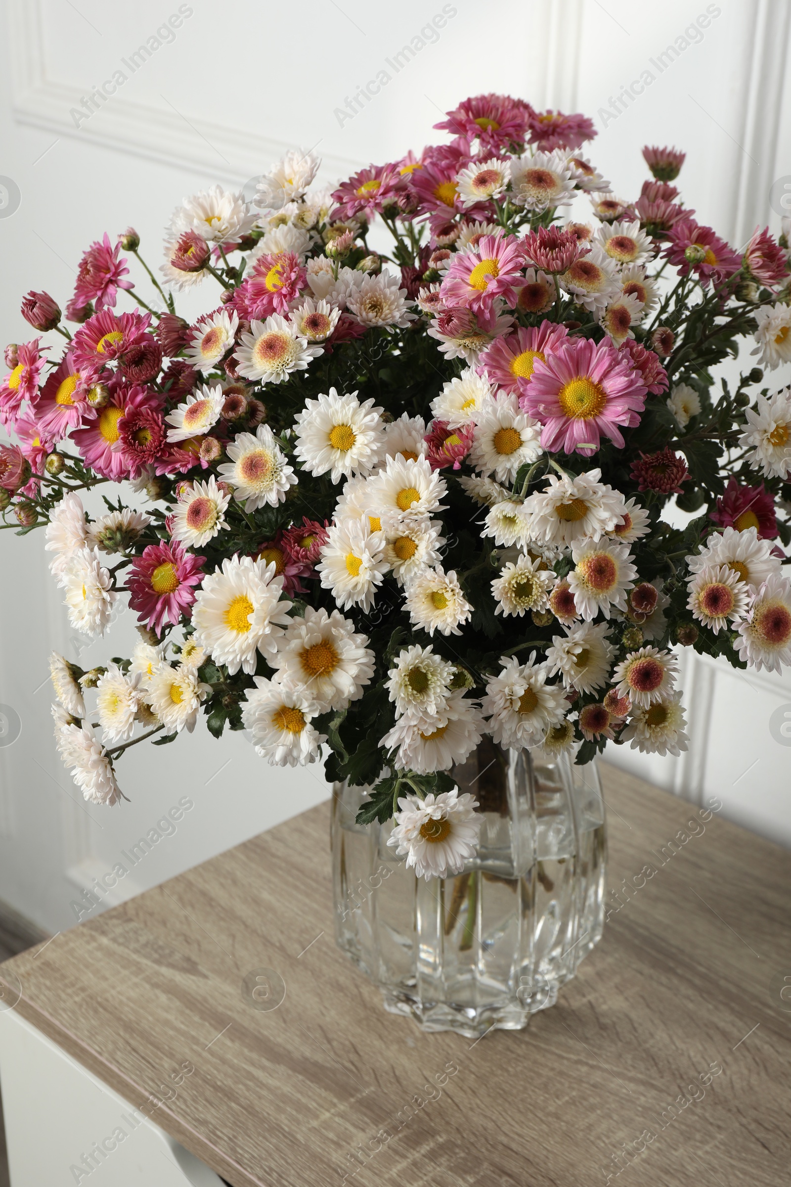 Photo of Vase with beautiful flowers on wooden nightstand, closeup