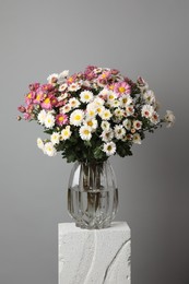 Photo of Vase with beautiful flowers on concrete block against gray background