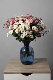 Photo of Vase with beautiful flowers on wooden nightstand against gray background