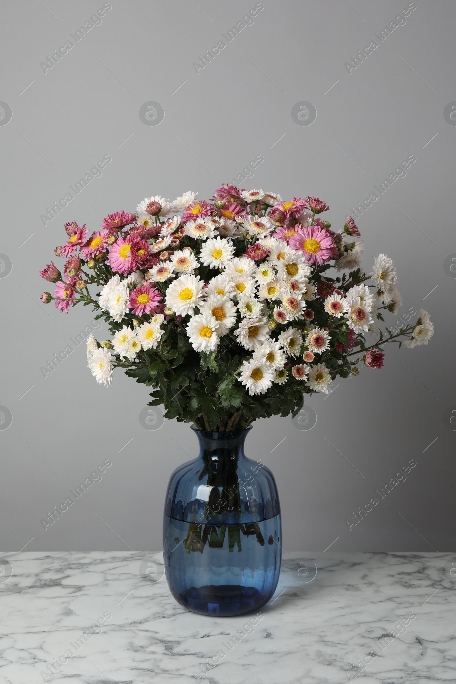 Photo of Vase with beautiful flowers on white marble table against gray background