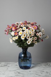 Photo of Vase with beautiful flowers on white marble table against gray background