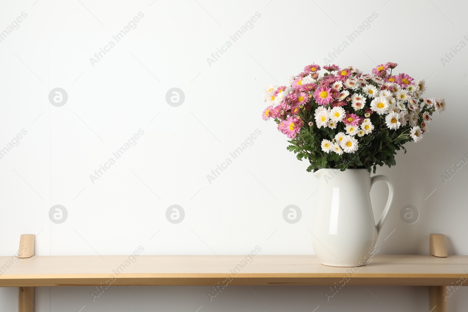 Photo of Vase with beautiful flowers on wooden shelf near white wall, space for text