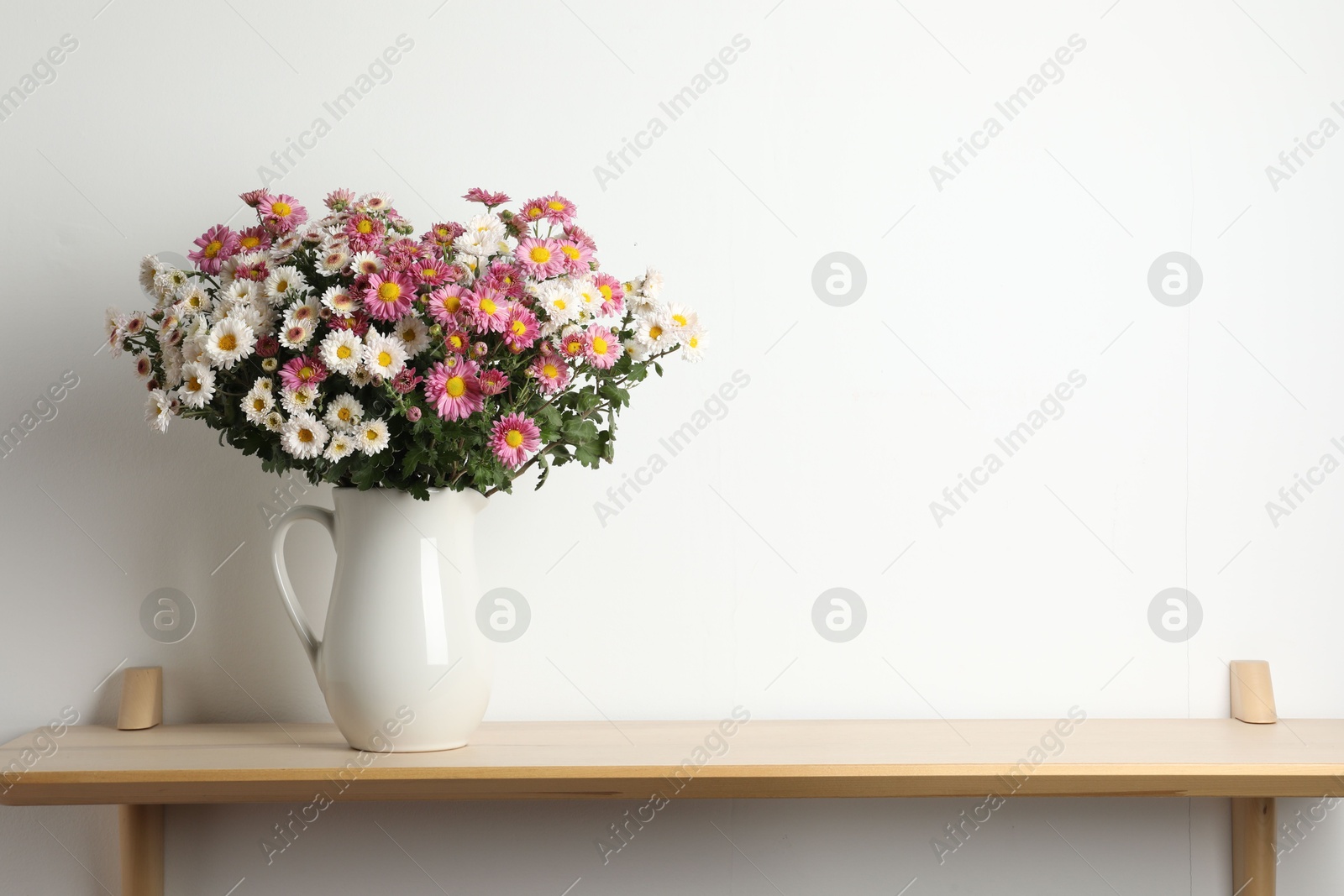 Photo of Vase with beautiful flowers on wooden shelf near white wall, space for text