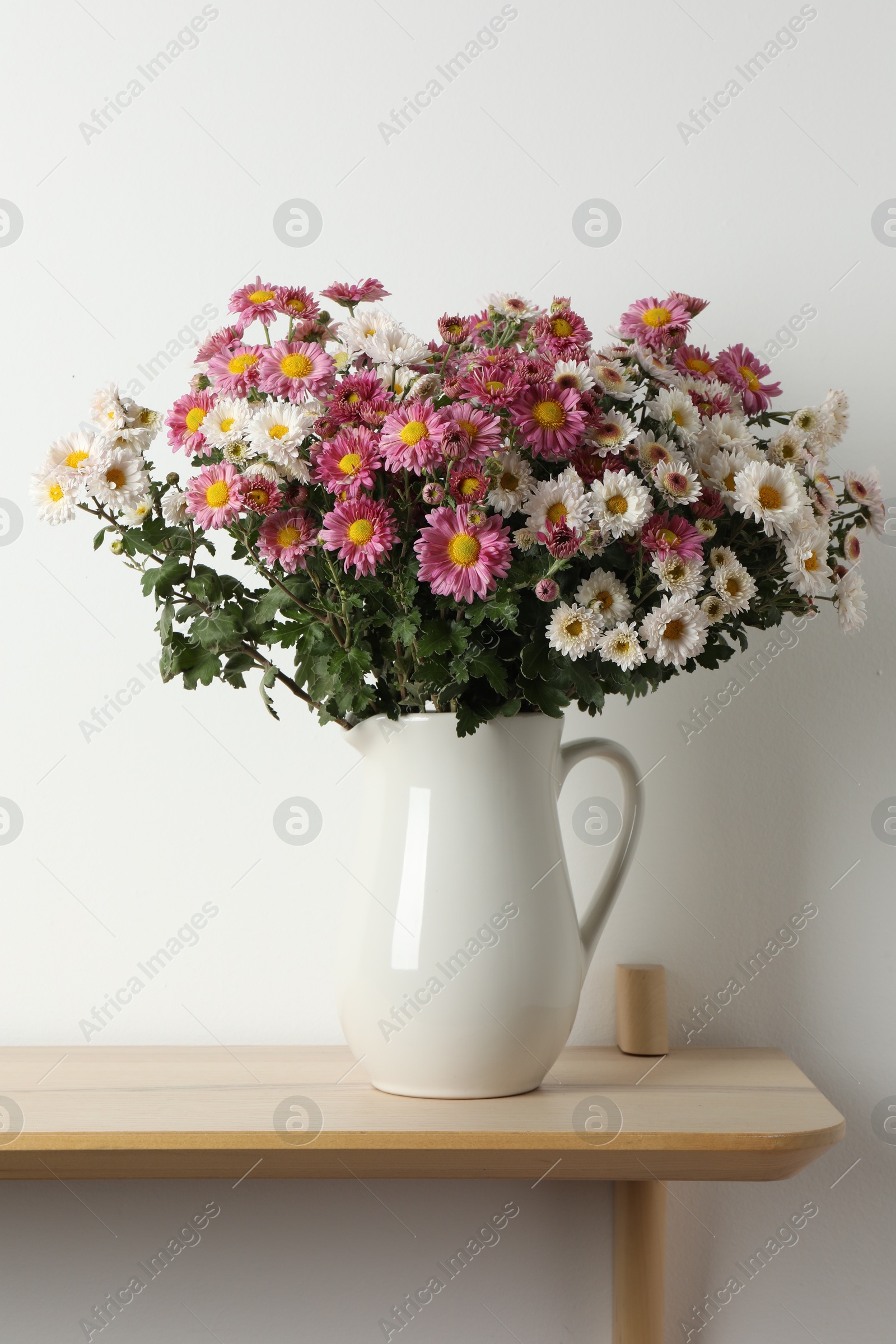 Photo of Vase with beautiful flowers on wooden shelf near white wall