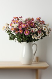 Photo of Vase with beautiful flowers on wooden shelf near white wall