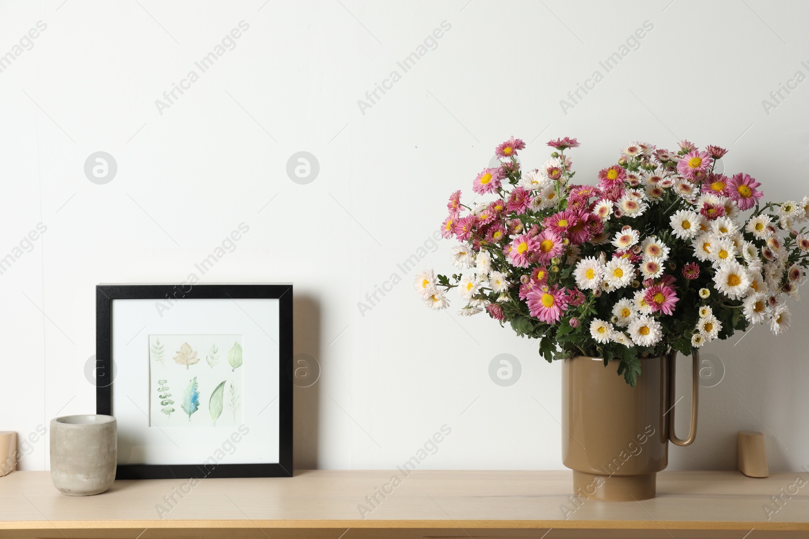 Photo of Vase with beautiful flowers and other decor on wooden shelf near white wall