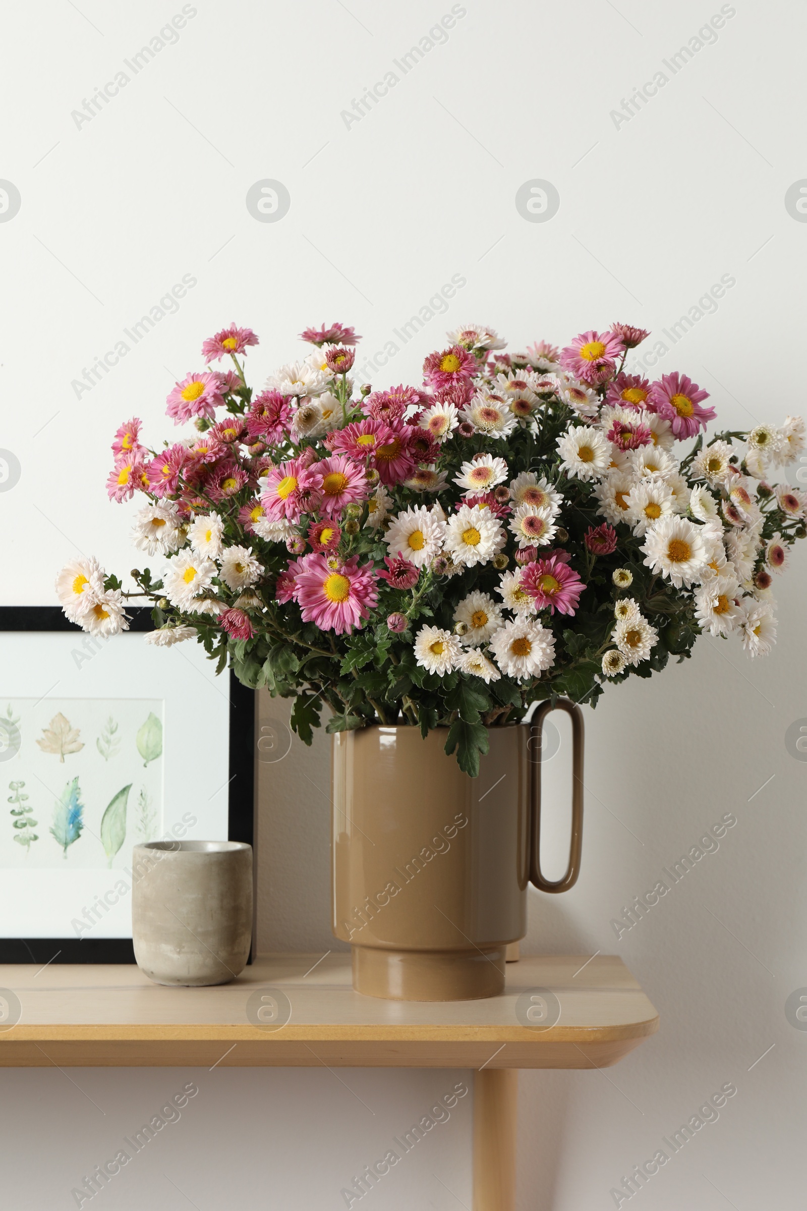 Photo of Vase with beautiful flowers and other decor on wooden shelf near white wall