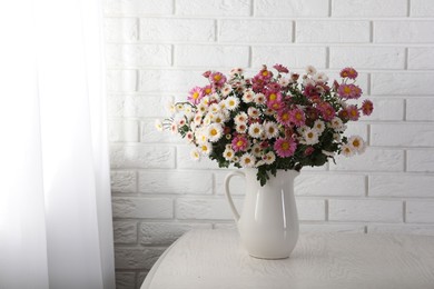 Photo of Vase with beautiful flowers on wooden table near white brick wall