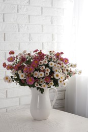 Photo of Vase with beautiful flowers on wooden table near white brick wall