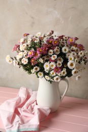 Photo of Vase with beautiful flowers and cloth on pink wooden table