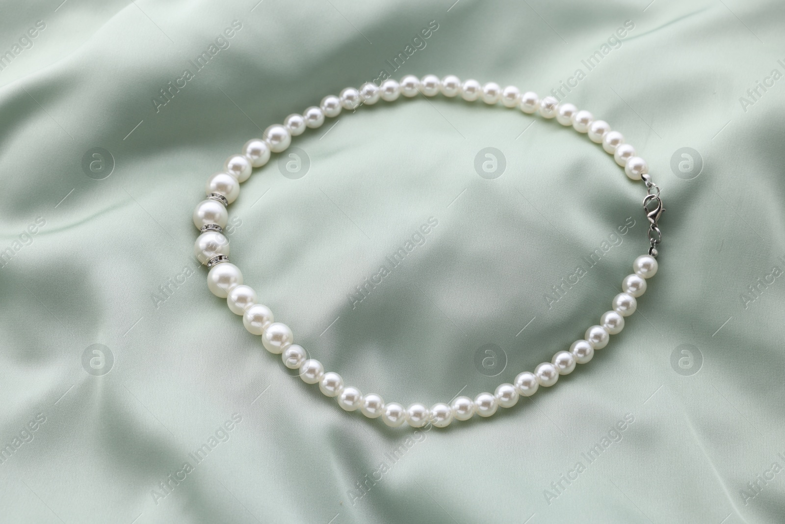 Photo of Beautiful pearl necklace on light green cloth, top view