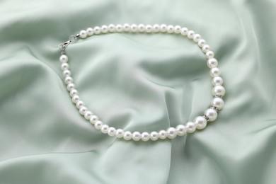 Photo of Beautiful pearl necklace on light green cloth, top view