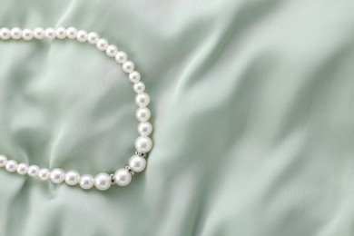 Photo of Beautiful pearl necklace on light green cloth, top view. Space for text