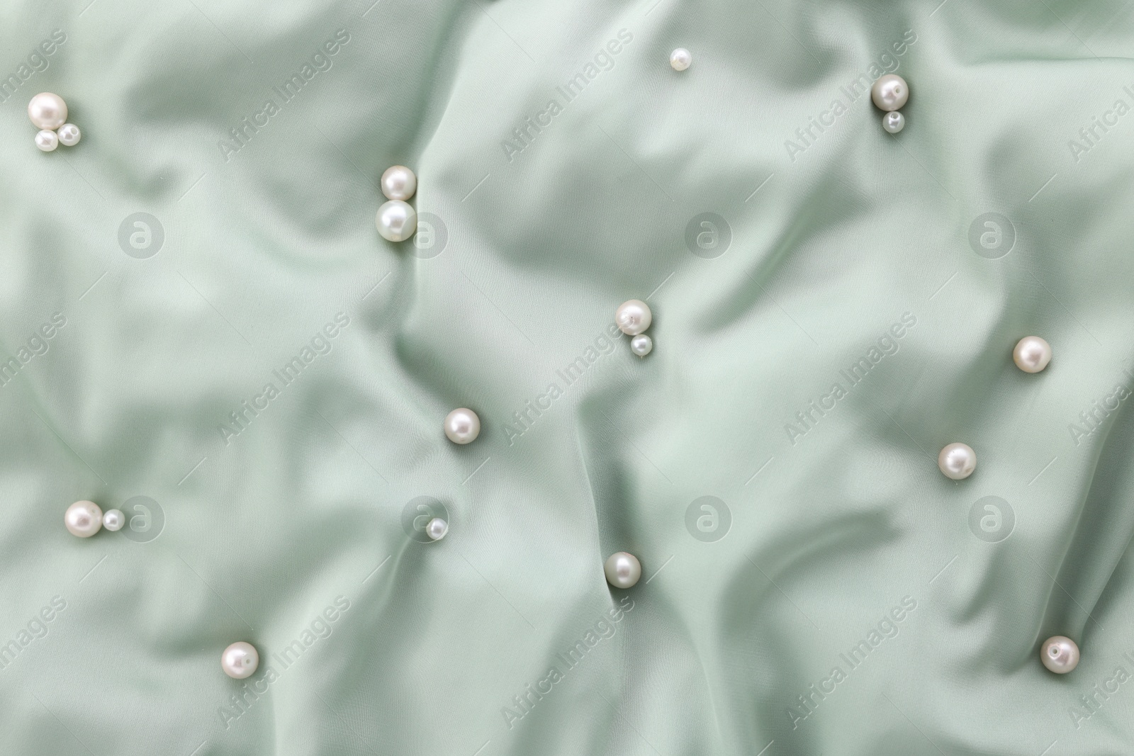 Photo of Many shiny pearls on light green cloth, top view