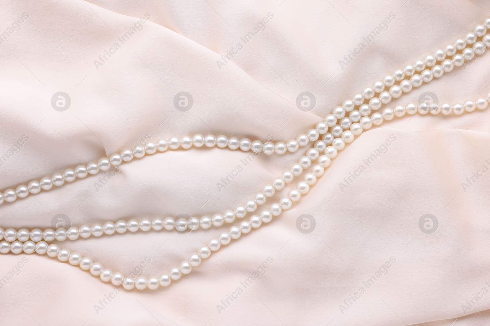 Photo of Beautiful pearl necklace on beige cloth, top view