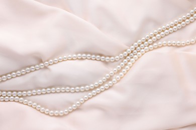 Photo of Beautiful pearl necklace on beige cloth, top view