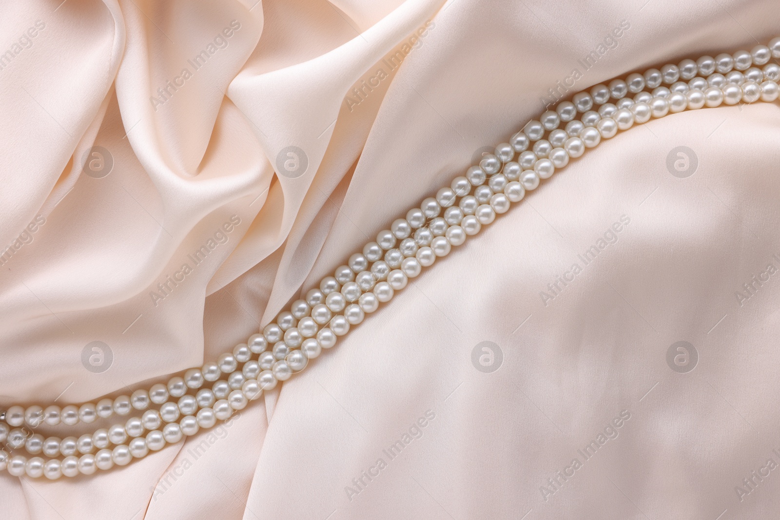 Photo of Beautiful pearl necklace on beige cloth, top view