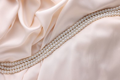 Photo of Beautiful pearl necklace on beige cloth, top view