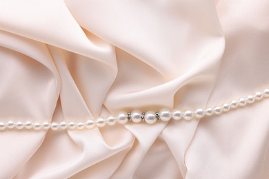 Photo of Beautiful pearl necklace on beige cloth, top view