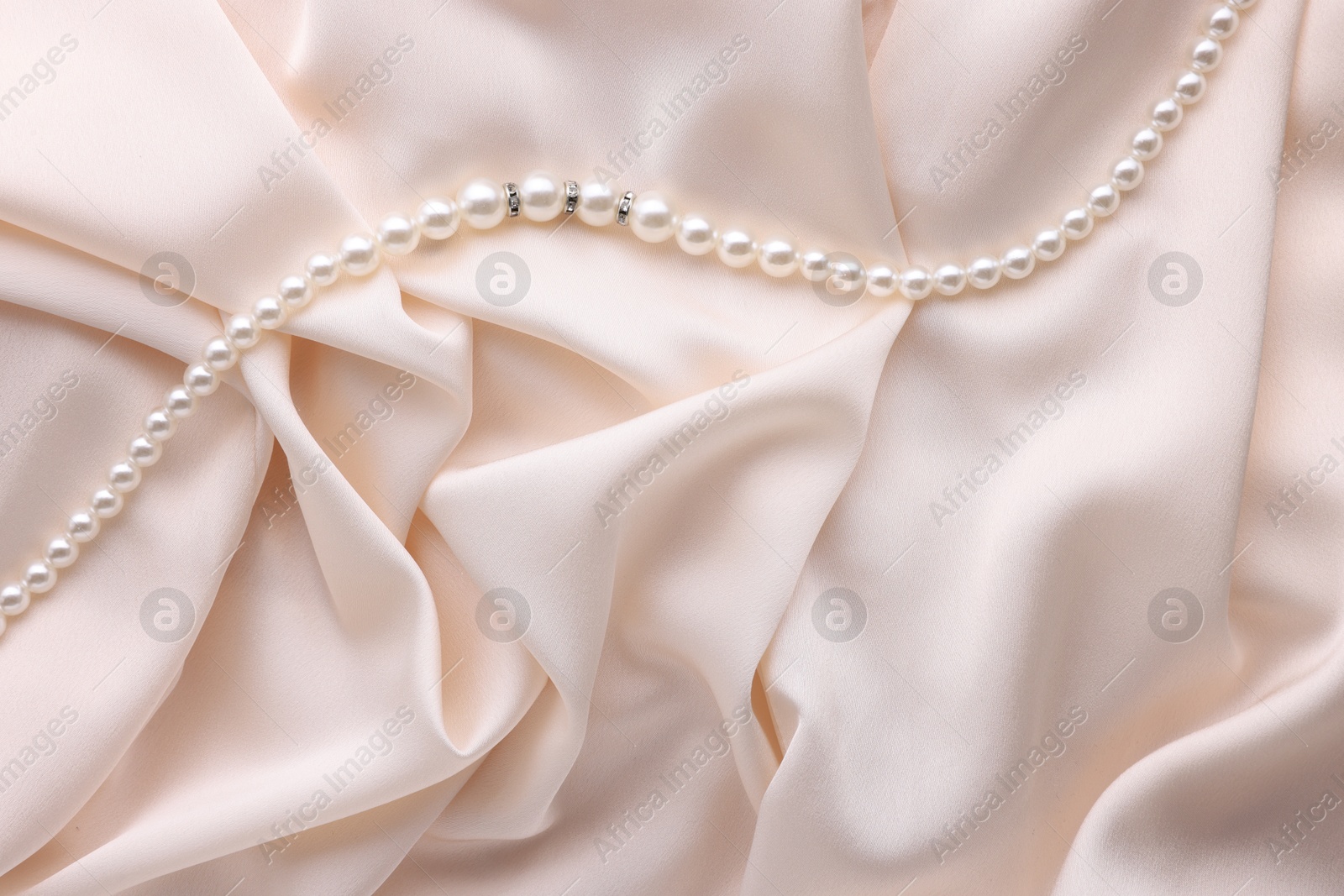 Photo of Beautiful pearl necklace on beige cloth, top view. Space for text