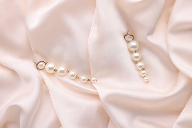 Photo of Beautiful pearl earrings on beige cloth, top view