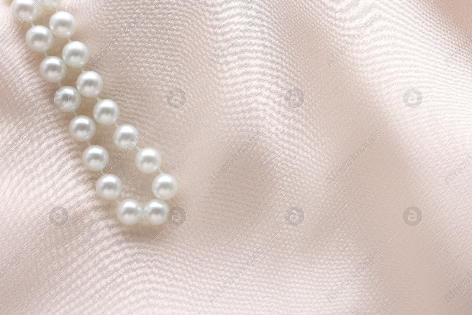 Photo of Beautiful pearl necklace on beige cloth, top view. Space for text