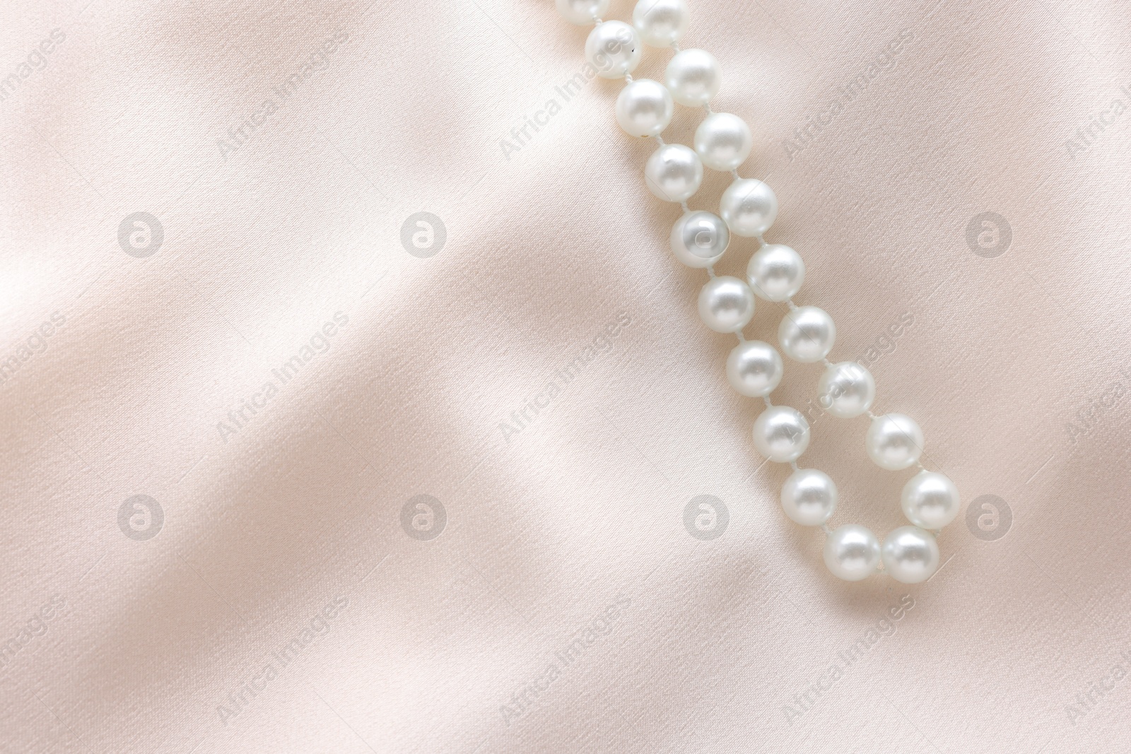 Photo of Beautiful pearl necklace on beige cloth, top view. Space for text