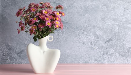 Photo of Stylish vase with beautiful flowers on pink wooden table. Space for text