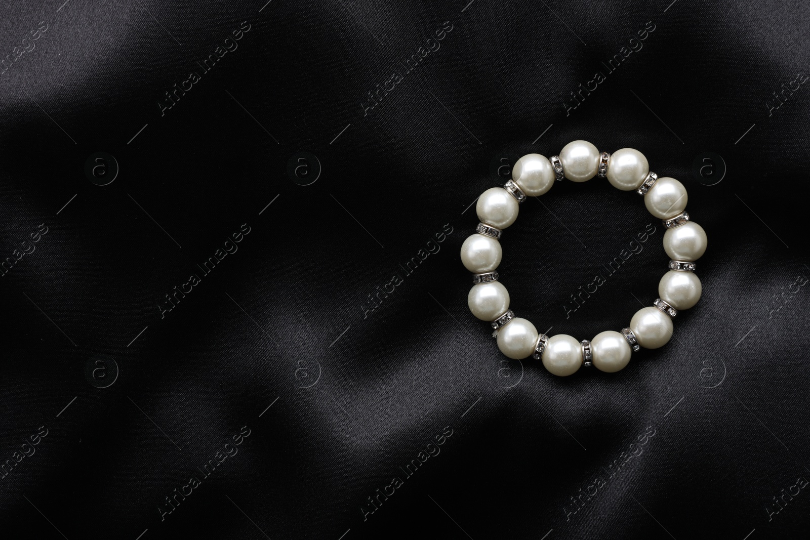 Photo of Beautiful pearl bracelet on black cloth, top view. Space for text