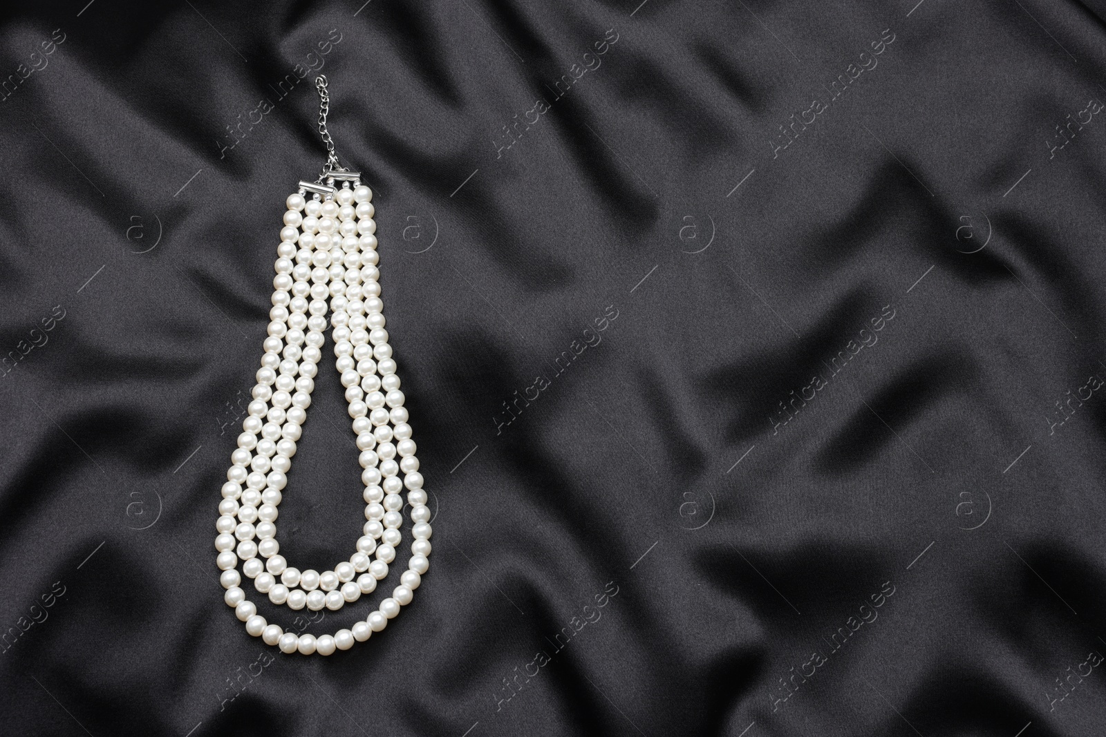 Photo of Beautiful pearl necklace on black cloth, top view. Space for text