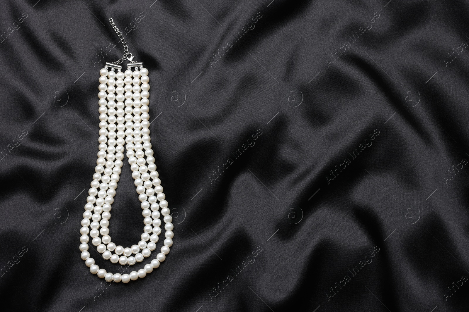 Photo of Beautiful pearl necklace on black cloth, top view. Space for text