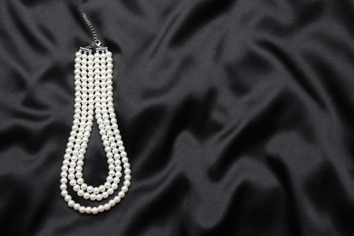 Photo of Beautiful pearl necklace on black cloth, top view. Space for text