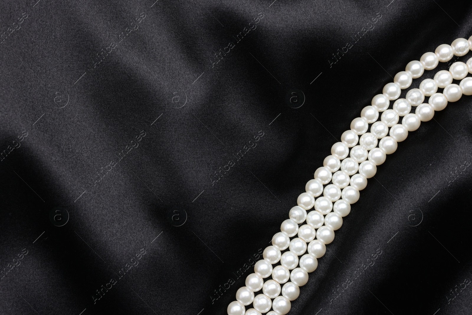 Photo of Beautiful pearl necklace on black cloth, top view. Space for text