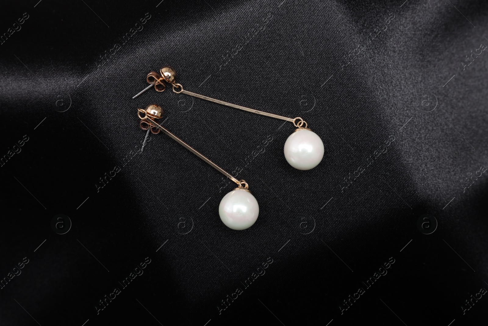 Photo of Beautiful pearl earrings on black cloth, top view