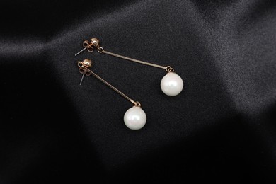 Photo of Beautiful pearl earrings on black cloth, top view