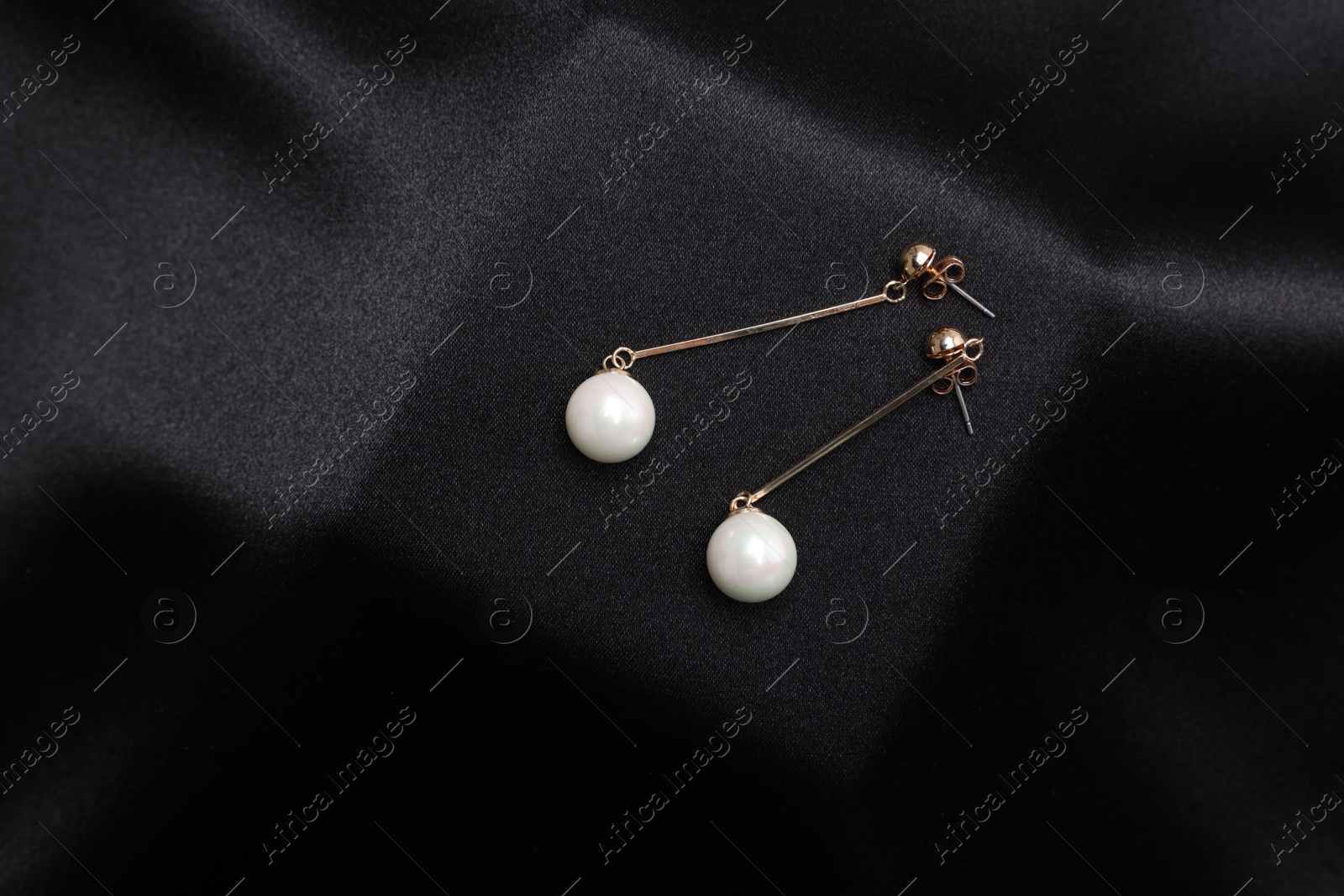 Photo of Beautiful pearl earrings on black cloth, top view