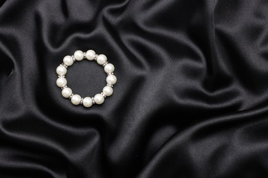 Photo of Beautiful pearl bracelet on black cloth, top view. Space for text