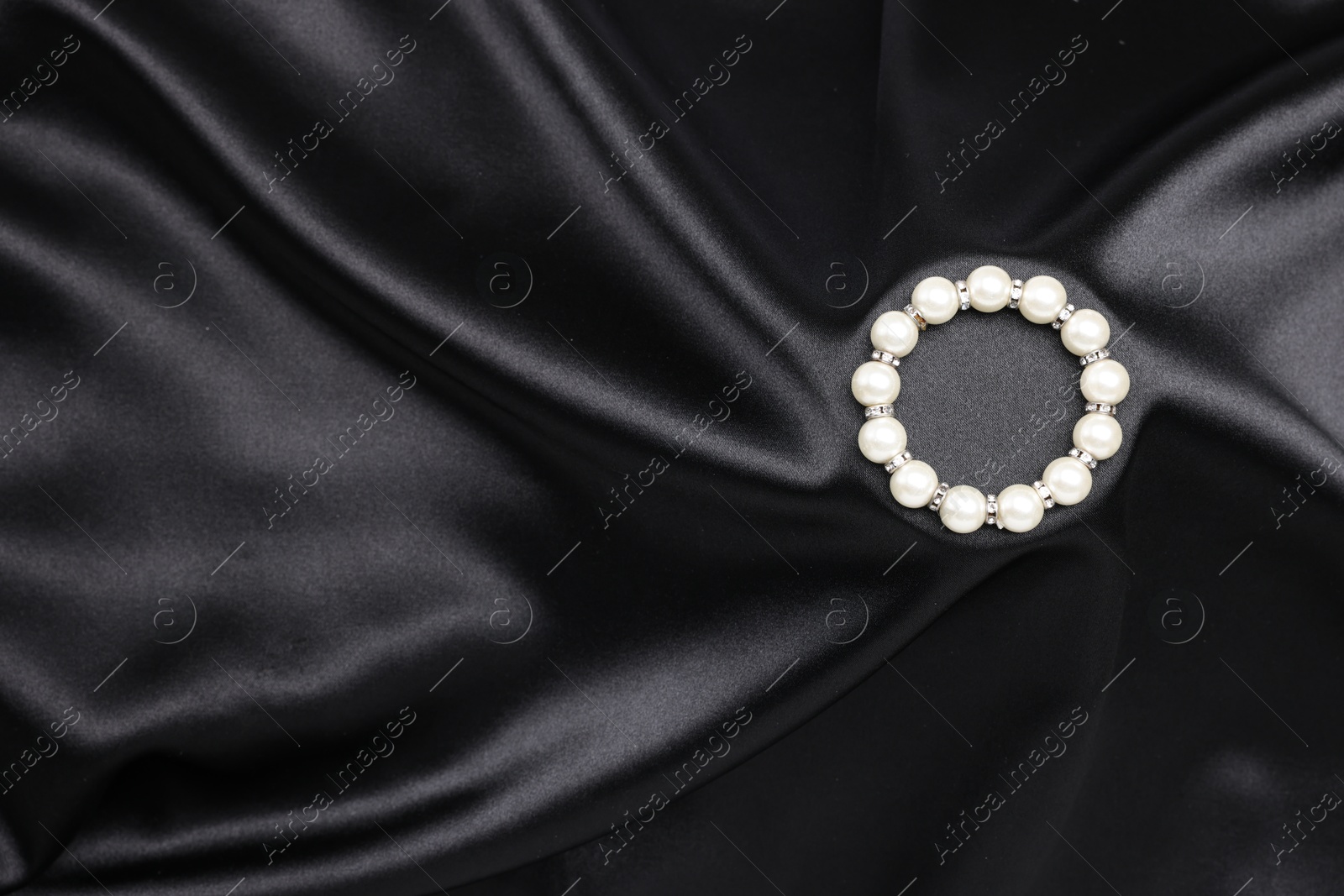 Photo of Beautiful pearl bracelet on black cloth, top view. Space for text