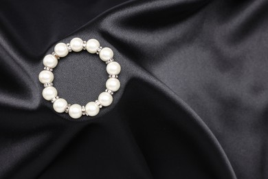 Photo of Beautiful pearl bracelet on black cloth, top view. Space for text