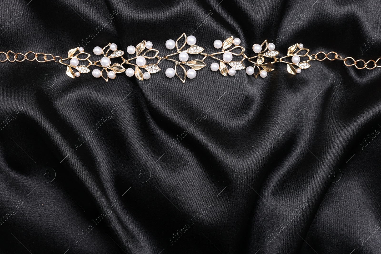 Photo of Beautiful bracelet with pearls on black cloth, top view. Space for text